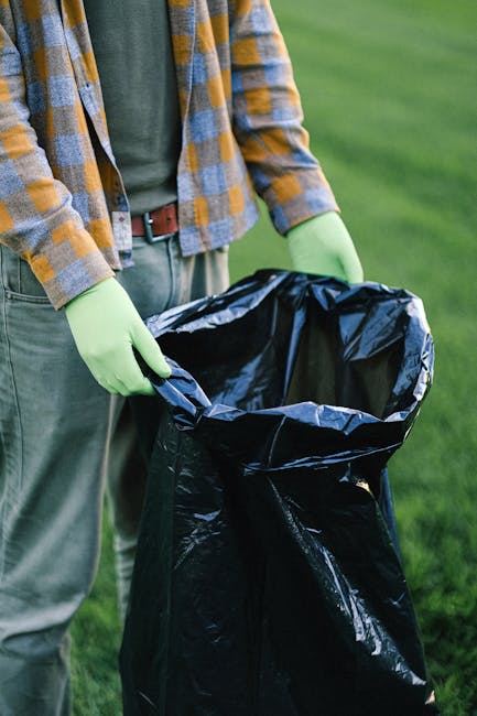 A large accumulation of black plastic rubbish bags stacked against a modern building with reflective metallic panels. The bags appear filled with waste materials and are tied at the top, some with vis